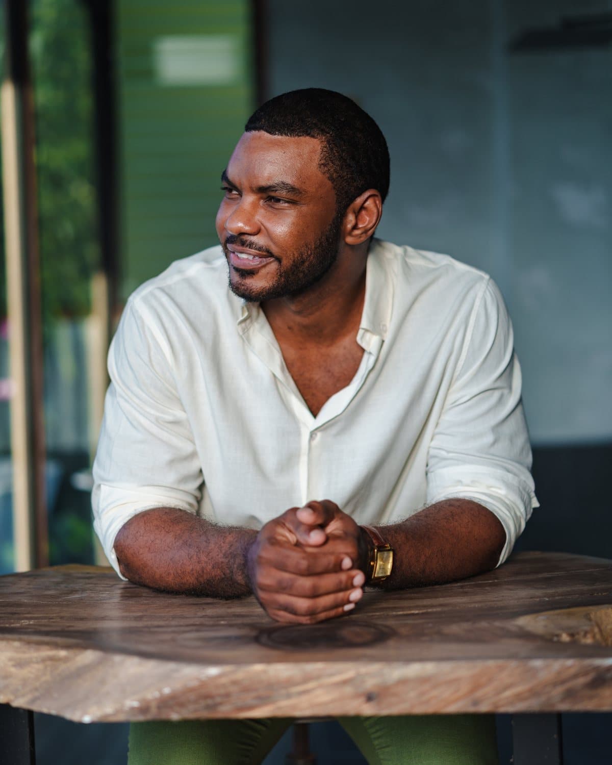 Dr. Edson Breedy at a wooden table in a white linen shirt, hands folded