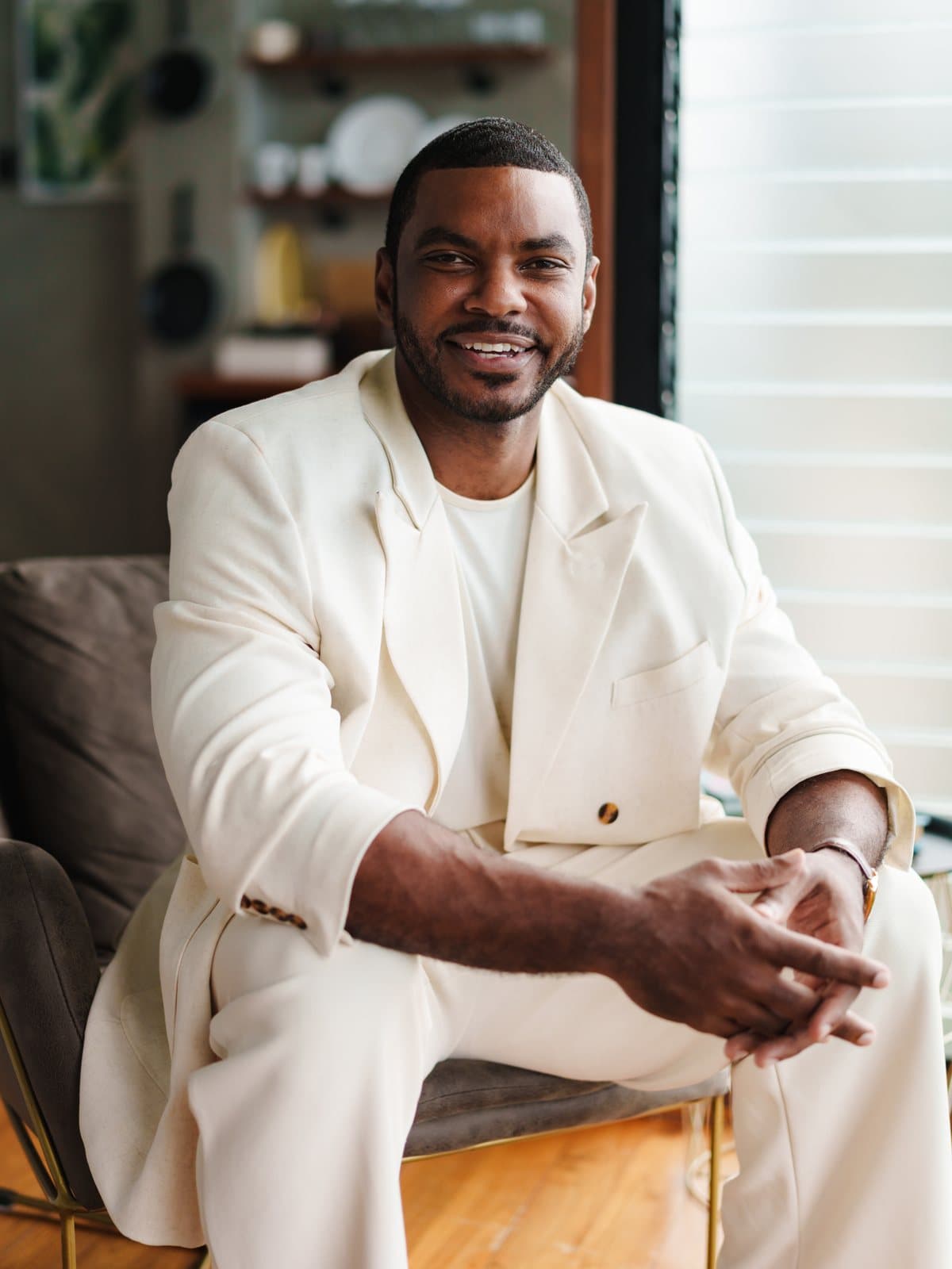 Dr. Edson Breedy seated in an armchair, in an ivory suit, smiling toward the camera